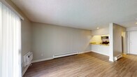 Located at 4982 S Ulster St in Denver, Colorado, this single-floor unit offers a functional and well-appointed layout. The open living area is finished with warm wood-look laminate flooring and neutral gray walls, creating a clean and versatile backdrop. A textured popcorn ceiling runs throughout the space, and a baseboard heating system lines the living room wall alongside a wall-mounted HVAC unit, ensuring year-round comfort. The kitchen is positioned adjacent to the living area and features stainless steel appliances — including a refrigerator, range, and microwave — paired with granite countertops and warm-toned tile backsplash. A breakfast bar peninsula provides a natural transition between the kitchen and living space. A hallway leads from the main living area to the bedroom and bathroom. The bedroom is a well-sized, quiet room with the same consistent wood-look flooring and neutral wall tones. The bathroom is outfitted with white cabinetry, a vanity with a framed mirror, and Hollywood-style lighting above. Adjacent to the bathroom is a closet with built-in shelving, offering practical storage. Recessed lighting in the kitchen adds warmth, while the overall design prioritizes a clean, move-in-ready aesthetic throughout.