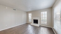 This single-floor residence offers a well-organized and functional layout designed for comfortable everyday living. The open-concept living area greets you upon entry with warm hardwood-style flooring, neutral-toned walls, and a textured ceiling. A ceiling fan with integrated lighting provides both comfort and illumination. The kitchen is accessible via a pass-through peninsula counter, fitted with white cabinetry, a stainless steel sink, and black appliances including a microwave and range. A separate view of the kitchen reveals additional cabinetry, a full-size refrigerator, and ample counter space in a clean, all-white finish. The living room features a fireplace as a focal point, adding character to the space, and receives natural light through windows with blinds. Bedrooms are carpeted for comfort, each equipped with ceiling fans and access to natural light through windowed doors. The bathroom is finished in a bright white palette, featuring a single-sink vanity with a large mirror, a toilet, and a tub-shower combination enclosed in white tile. Throughout the residence, the consistent use of neutral tones and practical finishes creates a cohesive, move-in-ready environment.