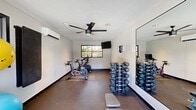 This fitness center in Dublin, California, is a thoughtfully designed single-story space built to support a well-rounded workout routine. The interior features durable rubber-composite flooring throughout, providing cushioning and traction suitable for a variety of exercises. Recessed lighting combined with a ceiling fan ensures the space remains well-lit and climate-controlled, complemented by a wall-mounted mini-split air conditioning unit for year-round comfort.

The room is divided into functional workout zones. A dedicated cardio area houses multiple stationary cycling bikes positioned beneath a wall-mounted flat-screen television, making indoor cycling sessions engaging and convenient. Adjacent to the cardio zone, a full rack of hex dumbbells in graduated weights provides ample options for strength training, accompanied by an adjustable workout bench. Exercise and stability balls are also available, adding versatility to the equipment offerings.

Large floor-to-ceiling mirrors line portions of the walls, enhancing the sense of space while allowing users to monitor their form. Expansive glass doors open directly to an outdoor pool area, flooding the interior with natural light and offering views of the surrounding community. A secondary window further contributes to the bright, open atmosphere of this practical and well-appointed fitness space.