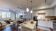 This single-story residence is thoughtfully designed with a cohesive aesthetic that blends modern finishes with a warm, inviting atmosphere. The open-concept kitchen serves as a central hub, featuring white shaker-style cabinetry, granite countertops, a stone tile backsplash, and stainless steel appliances including a refrigerator, dishwasher, and microwave. A kitchen island with seating for two provides additional prep and dining space, illuminated by a pair of pendant lights suspended from above. Track lighting complements the overall brightness of the kitchen.

The living area flows naturally from the kitchen and is anchored by a ceiling fan, a large window that brings in natural light, and ample space for comfortable seating arrangements. Dark hardwood flooring runs throughout the main living spaces, adding richness and continuity.

The bedroom offers a restful retreat with a walk-in closet, a window with views of greenery, and accent wall detailing. Two bathrooms serve the residence: one featuring a walk-in glass-enclosed shower with tile surround and granite vanity, and the other offering a soaking tub with shower combination, tile flooring, and a matching granite vanity. Both bathrooms are finished with white cabinetry and framed mirrors.