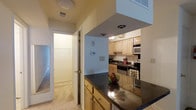 This single-floor residence at Village East Apartments offers a well-organized layout designed for comfortable everyday living. The kitchen is a central highlight, featuring dark granite-style countertops that contrast elegantly with the light wood cabinetry above and below. A peninsula counter extends the workspace, providing additional prep area and serving as a natural divider between the kitchen and adjacent spaces. The kitchen is equipped with stainless steel appliances, including a built-in microwave, dishwasher, and range, while recessed lighting overhead ensures a well-lit cooking environment. Upper cabinetry extends to the ceiling, maximizing storage capacity throughout. A hallway visible from the kitchen leads to a walk-in closet, offering generous storage space with built-in shelving and a rod for hanging garments. The flooring transitions from the kitchen area to plush carpeting in the adjacent rooms, adding warmth to the living spaces. A programmable thermostat is conveniently mounted on the wall, allowing for easy climate control. The overall ambiance is clean, neutral, and practical, making this a functional and inviting everyday living space.
