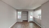 Located at 3210 Lynn Ridge Dr in Raleigh, NC, this single-floor home offers a well-organized layout with modern finishes throughout. The kitchen is a standout feature, designed in a galley style with white cabinetry, granite-look countertops, stainless steel appliances including a refrigerator, electric range, and built-in microwave, plus a stainless steel sink. Light wood-look flooring runs through the kitchen, complementing the bright, clean aesthetic. The main living and dining areas are finished with rich, dark wood-look flooring and neutral gray walls, creating a warm and cohesive atmosphere. Natural light filters in through multiple windows with blinds, offering views of the surrounding greenery. A built-in shelving unit provides convenient storage, while a glass-panel door leads directly to an outdoor area. A dedicated laundry area includes an in-unit washer, adding everyday practicality. The bedroom is generously proportioned with a large window and the same dark wood-look flooring. The bathroom features a full tub-and-shower combination with classic white square tile surround and chrome fixtures. Textured ceilings are present throughout, and the overall design reflects a clean, updated interior ready for comfortable living.