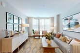 This thoughtfully laid-out 1-bedroom, 1-bathroom residence offers a seamless blend of modern design and functional living across a single floor. The open-concept layout connects the kitchen and living room, creating a bright and cohesive space ideal for everyday living and entertaining.

The kitchen is a standout feature, boasting quartz countertops, a large island with an integrated stainless steel sink, white lower cabinetry paired with warm wood upper cabinets, and a full suite of stainless steel appliances including a French door refrigerator, range, and microwave. A decorative wall-mounted rack adds a stylish accent near the entryway.

The living room is bathed in natural light through oversized windows dressed with sheer white curtains, offering views of the surrounding urban streetscape. Warm hardwood-style flooring runs throughout the common areas, contributing to the space's inviting ambiance.

The bedroom is a tranquil retreat featuring multiple large windows with adjustable blinds, allowing for flexible light control. The bathroom includes a glass-enclosed walk-in shower with floor-to-ceiling tile work and polished chrome fixtures, exuding a clean, contemporary aesthetic.

A dedicated closet provides practical storage, completing this efficiently designed and stylishly appointed residence.