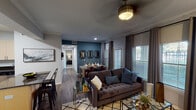 This well-designed single-floor residence showcases a cohesive contemporary aesthetic highlighted by rich hardwood-style flooring, crown molding, and a bold teal accent wall that flows through the living, dining, and bedroom areas. The open-concept living room is anchored by a classic white fireplace with mantel, crown molding details, and warm neutral walls, creating an inviting atmosphere ideal for relaxing or entertaining. A ceiling fan with a brushed gold finish adds a refined touch overhead. The adjacent dining area benefits from abundant natural light through large windows with blinds and floor-length curtains, complemented by decorative wall mirrors that enhance the sense of space. The kitchen is outfitted with stainless steel appliances including a refrigerator, range, and microwave, paired with light-toned cabinetry, dark granite countertops, and a classic subway tile backsplash. The bedroom continues the teal accent wall theme and features a ceiling fan, plush carpeting, and a bright window with outdoor views. Two bathrooms serve the residence — one with a soaking tub and shower combination and wood-look flooring, and a second with a tub-shower combo, vanity with cabinet storage, and a large mirror. Throughout, the space balances modern finishes with warm, layered design elements.