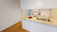 Located at 9091 Holder St in Cypress, CA, this single-floor residence offers a well-organized layout that balances functionality and comfort throughout its living spaces. The kitchen is efficiently designed in a galley style, featuring white cabinetry that extends to the upper walls for generous storage, light-toned laminate countertops, a stainless steel double sink, white electric range with coil burners, a built-in microwave, and a dishwasher. Wood-style flooring runs through the kitchen and flows into the main living areas, lending warmth and continuity to the space. A peninsula counter opens the kitchen toward the living area, creating an accessible and connected layout. The living room is bright and open, benefiting from a large window fitted with vertical blinds that allow natural light to filter in, complemented by a wall-mounted air conditioning unit. The bedrooms offer soft carpeted flooring, warm neutral-toned walls, and textured ceilings, providing a quiet and comfortable retreat. The bathroom is clean and well-appointed, featuring wood-style flooring, a full tub-and-shower combination with white tile surround, a vanity with matching light countertops, white cabinetry, and a sizeable mirror. Throughout the unit, consistent neutral tones, white trim, and textured ceilings create a cohesive and understated aesthetic.