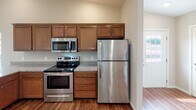This single-floor residence offers a thoughtfully designed open-concept layout that connects the kitchen and living areas seamlessly. The kitchen is well-equipped with warm-toned wood cabinetry, granite-style countertops, stainless steel appliances including a refrigerator, electric range, and built-in microwave, along with a central island with a sink that overlooks the main living space. Vaulted ceilings in the open living and kitchen area add a sense of spaciousness, while recessed lighting provides bright, even illumination throughout. Rich hardwood-style flooring runs through the main living areas, contrasted by plush carpeting in the bedrooms, each of which features a ceiling fan and windows fitted with blinds that allow for natural light. A sliding glass door in one room opens to an outdoor area, providing a connection to the exterior. The bathrooms include a full bath with a tub-shower combination and wood-style flooring, as well as a second bathroom featuring a standalone walk-in shower with built-in shelving and a linen closet nearby for added storage. Neutral wall tones and clean white trim are consistent throughout, lending the space a cohesive and move-in-ready aesthetic.