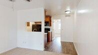 Located in Tucson, Arizona, this single-floor, one-bedroom, one-bathroom unit offers a well-organized layout designed to maximize every square foot. The living and kitchen areas feature warm hardwood-style flooring that flows throughout the common spaces, creating a cohesive and easy-to-maintain interior.

The kitchen is equipped with rich honey-toned wood cabinetry, open corner shelving, and light marble-patterned countertops. Black appliances — including a refrigerator, electric range, over-the-range microwave, and dishwasher — provide a clean, contrasting aesthetic. A pass-through window connects the kitchen to the living area, enhancing the sense of openness.

The bedroom is carpeted for comfort and features a ceiling fan, a window with blinds that allows natural light and views of the surrounding Tucson landscape, and notably, two separate sliding-door closets offering generous storage capacity.

The bathroom continues the warm wood cabinetry theme, with a marble-style countertop vanity, a large mirror, and hardwood-style flooring. A thermostat is conveniently accessible in the hallway just outside.

Throughout the unit, crisp white walls and trim contribute to a bright, clean ambiance, making this a practical and well-appointed Tucson residence.