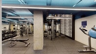 This fitness center is a fully outfitted, single-floor gym designed to support a wide range of workout routines. The space features an industrial aesthetic, with exposed ductwork and structural columns painted in a striking deep blue, complemented by sleek linear LED lighting that runs across the ceiling to provide consistent, bright illumination throughout. The flooring throughout the gym consists of durable rubber tiles, offering both safety and comfort during exercise. The strength training area is well-appointed with a variety of machines, including cable systems, Smith machines, multi-function racks, and a full dumbbell rack with accompanying adjustable benches. A standout design feature is a large textured black-and-white accent wall near the central training station, adding a bold visual element to the space. Mirrored walls are incorporated in key areas, enhancing the sense of openness. A dedicated area houses additional selectorized strength machines for targeted muscle training. The gym also includes cardio equipment and open floor space for functional training. A water fountain station and waste disposal area are conveniently located near an exit. Vintage sports posters are displayed on the walls, adding character and a nod to athletic heritage throughout the facility.