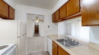 This single-floor residence offers a well-organized layout with a practical flow between living, sleeping, and utility spaces. The kitchen is equipped with warm oak cabinetry providing ample upper and lower storage, light countertops, a stainless steel sink, a dishwasher, and a refrigerator. Wood-look vinyl flooring runs through the kitchen and main hallway, lending durability and a cohesive look to the common areas. A central hallway connects the main rooms, featuring panel doors with brass hardware throughout.

The bedrooms are carpeted for comfort and each includes a ceiling fan with light fixture. Windows fitted with vertical blinds allow for natural light and privacy control. At least one bedroom features a walk-in-style closet with built-in shelving, offering practical storage solutions.

The bathroom presents a classic design with small square tile flooring, a vanity with wood cabinetry and a light countertop, a wall mirror, and a full-size soaking tub with an overhead shower. A separate door configuration provides added functionality and privacy within the bathroom area.

The dollhouse view confirms a spacious, rectangular floor plan that efficiently organizes the kitchen, living area, bedrooms, and bathrooms in a clear, accessible arrangement ideal for everyday living.