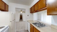 This single-floor residence offers a well-organized layout with a practical flow between living, sleeping, and utility spaces. The kitchen is equipped with warm oak cabinetry providing ample upper and lower storage, light countertops, a stainless steel sink, a dishwasher, and a refrigerator. Wood-look vinyl flooring runs through the kitchen and main hallway, lending durability and a cohesive look to the common areas. A central hallway connects the main rooms, featuring panel doors with brass hardware throughout.

The bedrooms are carpeted for comfort and each includes a ceiling fan with light fixture. Windows fitted with vertical blinds allow for natural light and privacy control. At least one bedroom features a walk-in-style closet with built-in shelving, offering practical storage solutions.

The bathroom presents a classic design with small square tile flooring, a vanity with wood cabinetry and a light countertop, a wall mirror, and a full-size soaking tub with an overhead shower. A separate door configuration provides added functionality and privacy within the bathroom area.

The dollhouse view confirms a spacious, rectangular floor plan that efficiently organizes the kitchen, living area, bedrooms, and bathrooms in a clear, accessible arrangement ideal for everyday living.