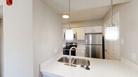 Located at 3301 River Park Dr in Fort Worth, TX, this one-bedroom, two-bathroom residence offers a well-organized layout across a single floor. The living room serves as the heart of the home, highlighted by a white-painted brick fireplace with a classic mantel, plush carpet flooring, a ceiling fan, and a window that brings in natural light with views of surrounding greenery. The kitchen is efficiently designed with white shaker-style cabinetry, white countertops, a subway tile backsplash, wood-look flooring, and stainless steel appliances including a range, over-the-range microwave, and refrigerator. The bedroom is a comfortable retreat featuring soft carpet, a ceiling fan, and a window overlooking outdoor foliage. It connects directly to a dedicated closet with built-in shelving for organized storage. The primary bathroom impresses with an extended white vanity, ample cabinet storage, dark wood-look flooring, and a large mirror with pendant lighting above. The second bathroom features a clean, white tiled tub-shower combination with wood-look flooring. A hallway connects the rooms, completing this efficiently designed and well-appointed residence.
