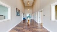 Located at 4811 Wildroot Ln in Fredericksburg, VA, this single-story community space offers a generous and thoughtfully designed layout spanning an expansive floor plan. The entrance is defined by a dramatic, soaring hallway with rich dark hardwood flooring, towering ceilings, and an elegant gold geometric pendant chandelier that sets a refined tone throughout. Neutral warm-gray walls and abundant natural light from a large end window create an open and welcoming atmosphere as you move through the corridor.

The main lounge area features coffered ceilings with pendant lighting, large windows with draping curtains offering outdoor views, and a comfortable arrangement of seating anchored by a patterned area rug — ideal for gathering and relaxing. Adjacent to the lounge is an intimate game and social nook with deep blue accent walls, built-in banquette seating, wall-mounted TV, and a collection of decorative mirrors, providing a cozy and engaging retreat.

A dedicated business center offers a clean, functional workspace with light gray walls, carpeted flooring, and workstations equipped with computers and a printer. The kitchen is well-equipped with white shaker cabinetry, dark stone countertops, stainless steel appliances, and hardwood flooring, finished with a bright window and tasteful pendant lighting.