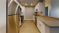 Located at 101 Rantoul Street in Beverly, Massachusetts, this single-floor unit offers a clean, modern aesthetic with thoughtfully updated finishes throughout. The open living areas are anchored by durable wood-style plank flooring in warm and cool tones, neutral taupe walls, and crisp white baseboards that lend a fresh, contemporary feel. Large windows invite natural light into the generously sized living spaces, offering views of the surrounding building exterior.

The galley-style kitchen is well-appointed with sleek white cabinetry, stainless steel appliances including a refrigerator, range, microwave, and dishwasher, complemented by neutral countertops and recessed lighting overhead. A pass-through opening connects the kitchen to the main living area, enhancing the sense of openness and flow.

The bedrooms are comfortably proportioned with ample wall space, wood-style flooring, and access to closet storage. The full bathroom features a tub-shower combination with clean white tile surround, wood-style flooring, and polished chrome fixtures.

A standout feature is the dedicated utility area housing a stacked washer and dryer unit alongside a vanity with an undermount sink and modern cabinetry, providing exceptional in-unit convenience. The textured ceiling treatment is consistent throughout, adding subtle depth to each room.