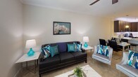 Located at 9511 Wes Kearney Way in Riverview, Florida, this single-floor residence offers a well-designed layout with a cohesive, neutral color palette throughout. The kitchen is a standout feature, showcasing rich dark cabinetry, light quartz countertops with under-cabinet LED accent lighting, stainless steel appliances including a refrigerator, range, and microwave, and a peninsula with bar seating — ideal for casual dining. Wood-look flooring and track lighting complete the space's modern aesthetic.

The living area is warm and inviting, featuring plush carpeting, crown molding, and a ceiling fan, creating a comfortable gathering space. Two well-proportioned bedrooms continue the soft, neutral tones with carpeted floors. The primary bedroom includes access to a dedicated walk-in closet with built-in shelving and hanging rods, offering generous storage. The second bedroom also benefits from a private closet.

The full bathroom is finished with a dark vanity, quartz countertop, and a tiled shower-tub combination. A dedicated in-unit laundry room with side-by-side washer and dryer hookups and wood-look flooring adds a practical and convenient amenity. Throughout the home, large windows invite natural light, contributing to the bright and airy atmosphere of this thoughtfully appointed residence.