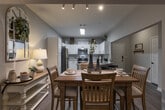 Located at 5402 FM-1488 in Magnolia, Texas, this single-story home offers a well-designed open-concept floor plan that seamlessly connects the kitchen, dining, and living areas. The kitchen is appointed with crisp white cabinetry featuring matte black hardware, granite countertops, stainless steel appliances including a dishwasher, and a functional breakfast bar with barstool seating — ideal for casual dining or entertaining. The adjoining dining area provides dedicated space for a full dining table and flows naturally into the living room, which boasts vaulted ceilings, a ceiling fan, hardwood-style flooring, and large windows with access to the outdoors, allowing for abundant natural light. Track lighting accents the dining space, adding a modern touch. The bedrooms are carpeted for comfort and feature closets and windows with natural light. The bathroom includes granite countertops, white cabinetry with modern hardware, and hardwood-style flooring, maintaining a consistent aesthetic throughout the home. Neutral gray tones on the walls complement the warm wood floors, creating a cohesive and welcoming ambiance across the entire residence.