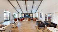 Located at 1994 US-72 E in Huntsville, Alabama, this single-story community clubhouse delivers an upscale, amenity-rich environment designed for socializing and recreation. The centerpiece is a generously proportioned main lounge featuring soaring vaulted ceilings accented by exposed dark wood beams, herringbone-patterned hardwood flooring, and abundant natural light streaming through large windows. Curated seating arrangements with cognac leather barrel chairs, a bold burgundy sofa, and mixed-pattern accent chairs create a warm, sophisticated atmosphere. A built-in media wall with flanking pendant lights anchors the lounge at one end, while bold artwork adds visual interest throughout.

An adjacent dining area showcases vivid teal cabinetry with granite countertops, dramatic woven pendant lighting, a wall-mounted TV, and a large communal wood table with leather chairs — ideal for gatherings or meetings. A café-style nook features banquette seating upholstered in deep burgundy, marble bistro tables, rattan chairs, and an eye-catching decorative wallcovering with framed deer illustrations.

The games room offers casual entertainment with arcade machines, skeeball, and a wall-mounted TV. Connecting hallways display additional curated artwork, and the overall design blends contemporary and eclectic elements cohesively throughout.