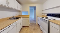 This single-floor 1-bedroom, 1-bathroom unit presents a clean, functional layout designed for comfortable everyday living. The living area is generously sized, featuring neutral wall-to-wall carpeting, crisp white walls, and a sliding vertical blind-covered window that allows natural light to fill the room. Baseboard heating units run along the walls, ensuring efficient climate control throughout the space. The galley-style kitchen is thoughtfully arranged with white cabinetry above and below, light wood-toned laminate countertops, a stainless steel sink, a white electric range, and a dishwasher. Tile flooring adds durability underfoot, and a pass-through window connects the kitchen to adjacent areas, enhancing the sense of openness. The bedroom offers comfortable carpeted flooring, neutral tones, and a wide double bi-fold closet that provides substantial storage capacity, along with baseboard heating for year-round comfort. The bathroom is straightforward and functional, featuring a full-size soaking tub and shower combination with clean white surrounds and chrome fixtures. Overall, the unit maintains a bright, neutral aesthetic throughout, making it a practical and move-in ready living space.
