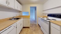 This single-floor 1-bedroom, 1-bathroom unit presents a clean, functional layout designed for comfortable everyday living. The living area is generously sized, featuring neutral wall-to-wall carpeting, crisp white walls, and a sliding vertical blind-covered window that allows natural light to fill the room. Baseboard heating units run along the walls, ensuring efficient climate control throughout the space. The galley-style kitchen is thoughtfully arranged with white cabinetry above and below, light wood-toned laminate countertops, a stainless steel sink, a white electric range, and a dishwasher. Tile flooring adds durability underfoot, and a pass-through window connects the kitchen to adjacent areas, enhancing the sense of openness. The bedroom offers comfortable carpeted flooring, neutral tones, and a wide double bi-fold closet that provides substantial storage capacity, along with baseboard heating for year-round comfort. The bathroom is straightforward and functional, featuring a full-size soaking tub and shower combination with clean white surrounds and chrome fixtures. Overall, the unit maintains a bright, neutral aesthetic throughout, making it a practical and move-in ready living space.