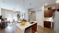This single-story residence at Hardy Yards in Houston, Texas offers a thoughtfully designed open-concept layout that seamlessly connects the kitchen, dining, and living areas. The kitchen serves as a central hub, anchored by a spacious island with a white quartz countertop, an undermount sink, and seating for casual dining. Rich dark-walnut cabinetry extends to the upper walls, complemented by subway tile backsplash and stainless steel appliances, including a French door refrigerator and dishwasher. Pendant lighting illuminates the island, while recessed lighting brightens the broader space.

The living area flows naturally from the kitchen and features wood-look flooring, a ceiling fan, and French doors that invite natural light and outdoor views. Neutral wall tones provide a warm, versatile backdrop throughout.

The bedrooms are carpeted and generously sized, with large windows dressed in sheer curtains and blinds that allow ample natural light. The primary bathroom is well-appointed with dark cabinetry, quartz countertops, a glass-enclosed walk-in shower with white tile surround, and wood-look flooring. A walk-in closet connects directly to the bathroom for added convenience. An in-unit laundry area adds practical functionality to this well-rounded residence.