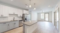 Located at 1148 N Main St in Jacksonville, FL, this well-appointed two-bedroom, two-bathroom residence offers a thoughtfully designed single-floor layout with a clean, contemporary aesthetic throughout. The open-concept living and kitchen area serves as the heart of the home, featuring light hardwood-style flooring, recessed lighting, and pendant lights over a central island with quartz countertops. The kitchen is fully equipped with stainless steel appliances — including a French door refrigerator, dishwasher, microwave, and range — complemented by shaker-style cabinetry and a classic subway tile backsplash. A ceiling fan anchors the living area, which receives natural light through large windows. Both bedrooms are carpeted and generously proportioned, each featuring a ceiling fan and windows with outdoor views of surrounding greenery. Two dedicated closets provide ample storage. The primary bathroom includes a double-sink vanity with gray cabinetry, a tub-shower combination with subway tile surround, and matte black fixtures. The second bathroom mirrors this modern style with a walk-in tiled shower and double vanity. The overall ambiance is bright, clean, and move-in ready.