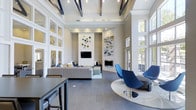 Located at 6805 West Bowles Avenue in Littleton, Colorado, this single-floor community space is a showcase of modern design and refined comfort. The interior immediately impresses with its soaring ceilings accented by bold dark exposed beams that contrast beautifully against crisp white surfaces, creating a dramatic yet welcoming atmosphere throughout.

The main gathering area is anchored by a sleek fireplace set into a floor-to-ceiling shiplap accent wall, flanked by a wall-mounted television, making it an ideal focal point for relaxation and socializing. A generously sized sectional sofa in neutral tones provides ample seating, while a pair of striking cobalt blue accent chairs positioned on a circular platform add a bold splash of contemporary flair.

Natural light pours in abundantly through tall, grid-paned windows that line the walls, framing views of the surrounding landscape and giving the space an open, airy quality. The floors are finished in wide-plank grey tile that complements the cool, sophisticated color palette of whites, greys, and blues throughout.

Curated artwork and decorative wall installations lend a gallery-like sensibility, while recessed and track lighting ensure the space is well-lit at all hours. A bar-height counter and seating along one edge offer an additional casual gathering spot, completing this thoughtfully designed and highly functional communal environment.