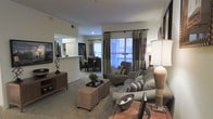 Located at 900 Waterford Forest Cir in Cary, NC, this single-floor residence offers a well-designed layout that balances comfort and functionality. The open-concept living area serves as the heart of the home, featuring plush carpeting underfoot and a warm, neutral color palette throughout. Large windows dressed with elegant striped drapes flood the space with natural light, creating a bright and welcoming atmosphere. The living room provides generous space for seating and entertaining, with smooth-flowing sightlines that connect seamlessly to the dining area beyond. A pass-through counter connects the living and dining spaces to the kitchen, which features light cabinetry and offers convenient visual access to the main living areas — ideal for both everyday living and hosting guests. The dining area is positioned near the windows, allowing residents to enjoy natural light during meals. A sliding glass door provides access to an outdoor balcony, extending the living space and offering views of the surrounding community. The overall ambiance is relaxed yet refined, with a cohesive design that emphasizes openness, natural light, and comfortable living throughout the home.