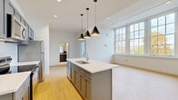 Located at 25 Public Square in Willoughby, Ohio, this thoughtfully designed one-bedroom, one-bathroom residence offers a efficient and modern living experience across a single floor. Light hardwood flooring flows throughout the unit, complementing the clean white walls and creating a bright, cohesive aesthetic.

The open-concept kitchen is a standout feature, centered around a spacious island with a white quartz countertop, undermount sink, and trio of sleek black pendant lights overhead. Gray shaker-style cabinetry lines both sides of the galley-style kitchen, paired with white subway tile backsplash and a full suite of stainless steel appliances including a range, microwave, refrigerator, and dishwasher.

The living room is generously proportioned, bathed in natural light from large multi-pane windows that frame views of the surrounding neighborhood. The bedroom offers a comfortable footprint with its own large windows and access to a dedicated closet.

The bathroom is elegantly appointed with a glass-enclosed walk-in shower, classic white penny tile flooring, bold green vertical wall tile, built-in shelving, and chrome fixtures. Additional spaces include a laundry room and utility room, rounding out the functionality of this well-planned residence.