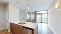 Located at 3420 Broadway Blvd in Kansas City, Missouri, this contemporary single-floor residence is designed with a clean, modern aesthetic and thoughtful attention to detail throughout. The open-concept kitchen is a standout feature, equipped with stainless steel appliances including a range, microwave, refrigerator, and dishwasher. Warm wood-toned cabinetry pairs with white quartz countertops and a double-basin sink, while pendant lighting adds a refined touch. The kitchen flows seamlessly into the living area, which is bathed in natural light thanks to large sliding glass doors with vertical blinds and clerestory windows that frame city views. Light wood-style flooring extends throughout the main living spaces, creating a warm and cohesive feel. The bedrooms are well-proportioned, each featuring ceiling fans, additional windows, and access to outdoor views. The bathrooms are finished with neutral tile, wood-toned vanities, white quartz countertops, and brushed nickel fixtures — one featuring a tiled walk-in shower and another with a full soaking tub and shower combination. Wall sconces in the living area add a soft, welcoming ambiance. The overall design balances contemporary finishes with a bright, open atmosphere.