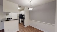 This single-story unit offers a thoughtfully designed layout that maximizes functionality across its living spaces. The living room serves as a central gathering area, featuring rich wood-style flooring, a ceiling fan with light fixture, and a marble-surround fireplace that adds a distinctive focal point. Natural light enters through multiple windows, and a front entry door provides direct access to the space.

Adjacent to the living room, a dedicated dining area is defined by a stylish pendant light fixture and a chair rail detail along the neutral gray walls, with wood-style flooring continuing seamlessly from the living space. The galley-style kitchen is efficiently arranged with white cabinetry, dark granite-style countertops, a mosaic tile backsplash, and stainless steel appliances including a refrigerator, range, and dishwasher.

The bedroom offers plush carpeting, a sliding door with vertical blinds that provides access to an outdoor area, and direct entry to the full bathroom. The bathroom includes white cabinetry, dark countertops, a single vanity sink with a large mirror, and a tiled tub-shower combination. A closet with louvered doors provides additional storage within the unit.