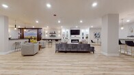 Located at 2 Walter Ave, this single-floor space showcases a thoughtfully designed open-concept layout that seamlessly connects multiple living and entertaining zones. Light wood-tone plank flooring runs throughout, lending a clean, contemporary feel to the entire space.

The central lounge area is anchored by a built-in entertainment wall finished in white, featuring a wall-mounted flat-screen TV, a sleek linear electric fireplace, and display shelving accented with decorative objects. Comfortable sectional and accent seating arrangements are positioned to take full advantage of this focal point.

Adjacent to the main lounge, a secondary seating area provides additional gathering space, with bold navy double doors serving as a striking architectural detail. Wall-mounted sconces and recessed lighting throughout ensure the space is well-lit and inviting.

A standout feature is the stylish wet bar, complete with a white quartz countertop, light wood cabinetry, a tile backsplash, floating shelves, gold-accented pendant lighting, and black leather bar stools with gold legs. A wall-mounted TV above the bar adds to its entertainment-ready appeal.

A large landscape mural adds a dramatic artistic element, while curated artwork and decorative accessories contribute to the space's polished, modern aesthetic. The open floor plan and generous proportions make this an ideal venue for both relaxed gatherings and lively entertaining.
