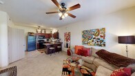 This well-designed one-bedroom, one-bathroom unit in Owasso, Oklahoma, makes efficient use of its single-floor layout. The open-concept living and kitchen area forms the heart of the space, where the kitchen stands out with rich, dark wood cabinetry extending to the ceiling, granite-style countertops, black appliances, and a breakfast bar with two barstool seats—ideal for casual dining. The kitchen flows naturally into the carpeted living area, which features a ceiling fan with light fixture and a window that allows natural light to fill the room.

The bedroom is a comfortable, well-proportioned retreat, also carpeted and equipped with a ceiling fan. A window provides additional natural light, while a dedicated closet offers practical storage. The room connects directly to the rest of the unit via a tiled hallway.

The bathroom features rich wood vanity cabinetry, a white countertop with sink, a framed mirror with overhead lighting, a wall-mounted cabinet for additional storage, and tile flooring. The overall color palette throughout is warm and neutral, creating a cohesive and inviting atmosphere across every room.