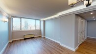 This elegantly updated high-rise unit offers a refined living experience with a cohesive modern aesthetic throughout. Warm hardwood-style flooring flows seamlessly across the entire space, complemented by soft blue-grey walls, crisp white crown molding, and recessed cove lighting that lends a polished, upscale ambiance.

The open living areas are generously proportioned, with large floor-to-ceiling windows framing sweeping panoramic city skyline views, flooding each room with abundant natural light. Wall-mounted sconce lighting adds a warm, architectural touch to the bedrooms and living spaces.

The kitchen is a standout feature, showcasing dark espresso lower cabinetry paired with white upper cabinets accented by frosted glass inserts. Gleaming granite countertops, a classic white subway tile backsplash, stainless steel appliances including a range, microwave, and dishwasher, and a recessed tray ceiling with integrated lighting complete this functional and stylish space.

The bathroom is finished with the same attention to detail, featuring white subway tile wainscoting, a decorative mosaic tile border, granite vanity countertop, dark wood cabinetry, and modern chrome fixtures. The overall layout, as seen in the dollhouse view, is well-structured and spacious, making efficient use of every area.