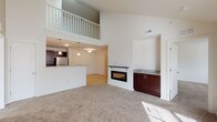 This two-floor residence offers an impressive sense of vertical space, anchored by a dramatic double-height living area with a second-floor balcony overlook framed by white railings. The living room features plush carpeting, an integrated linear fireplace with a granite-topped built-in cabinet, and an open connection to the kitchen and dining area that promotes a seamless flow throughout the main level. The kitchen is well-appointed with rich dark espresso cabinetry, granite countertops, light hardwood-style flooring, and a full suite of stainless steel appliances including a range, over-the-range microwave, dishwasher, and refrigerator. Pendant lighting above the kitchen bar adds a polished finishing touch. The bathrooms continue the cohesive design aesthetic with dark vanity cabinetry, white countertops, large mirrors, and hardwood-style flooring. In-unit washer and dryer hookups provide added convenience. The bedrooms are carpeted and bright, with natural light streaming through large windows. Generous closet space is found throughout, including a spacious walk-in closet with wire shelving systems. The upper level adds further versatility, completing a functional and well-designed two-story layout.