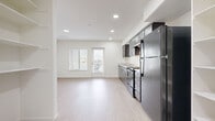 This studio presents a thoughtfully designed open-plan layout that maximizes every square foot of its single-floor footprint. Light wood-style flooring flows continuously throughout the space, lending a clean, cohesive aesthetic against crisp white walls and ceilings fitted with recessed lighting.

The kitchen runs along one wall and is a standout feature, outfitted with rich dark-espresso cabinetry — both upper and lower — paired with light stone-finish countertops. Full-size black appliances include a gas range, dishwasher, and refrigerator, making the kitchen as functional as it is visually striking. A single-basin sink and ample cabinet storage complete the setup.

The open living area is generously proportioned relative to the studio format, offering flexibility for varied furniture arrangements. Natural light enters through windows fitted with horizontal blinds, and a wall-mounted mini-split HVAC unit provides independent climate control. A dedicated electrical panel is neatly recessed into the wall.

The bathroom is accessible via a short hallway and features a clean, all-white interior with wood-style flooring, grab bars, and essential fixtures. A closet area is also accessible from the hallway, offering built-in storage. Overall, the space delivers a modern, functional design with a neutral palette suitable for a range of uses.