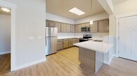 This well-appointed 2-bedroom, 2-bathroom residence in American Fork, Utah offers a thoughtfully designed single-level layout. The open-concept kitchen is a standout feature, showcasing warm taupe cabinetry with brushed nickel hardware, crisp white countertops, a peninsula with pendant lighting, and a full suite of stainless steel appliances including a refrigerator, electric range, and microwave. A skylight adds an inviting brightness to the kitchen area. Light wood-style flooring flows throughout the main living areas, complementing the neutral, airy color palette. The living room is generously sized, featuring a ceiling fan, a large window, and a glass door that brings in ample natural light. Both bedrooms are carpeted for comfort and include ceiling fans and windows that fill the rooms with natural light. The primary bedroom offers a notably spacious footprint with a closet for storage. The two bathrooms are cleanly finished with wood-look tile flooring, white surrounds, and vanities with white countertops. A dedicated in-unit laundry room provides added convenience, complete with overhead shelving and a full-size washer and dryer. A connecting hallway ties the layout together for a functional and cohesive flow throughout the home.