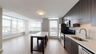 This contemporary single-floor residence delivers a clean, modern aesthetic with a thoughtfully designed open-concept layout. The kitchen serves as a central highlight, outfitted with dark espresso cabinetry, stainless steel appliances including a refrigerator, range, and over-the-range microwave, a subway tile backsplash, and light quartz countertops. A freestanding island provides additional prep and storage space, while light hardwood-style flooring extends seamlessly into the adjacent living area.

The living space is defined by expansive floor-to-ceiling windows that flood the interior with natural light and offer impressive elevated views of the surrounding cityscape. The open layout creates a generous sense of space and flow between the kitchen and living areas.

The bedrooms feature soft carpeting, neutral wall tones, and large windows that continue the theme of abundant natural light and urban views. Closet space is provided for practical storage needs.

Both bathrooms are finished with the same dark wood-toned cabinetry, white quartz countertops, undermount sinks, and light tile flooring, creating a cohesive and polished look throughout. Accessibility-friendly grab bars are also present.

Overall, this residence combines contemporary finishes, functional design, and striking city views to offer a refined and comfortable urban living experience.