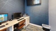 Located at 257 Pinecroft Dr in Taylors, SC, this compact single-room space functions as a well-appointed workstation area. The room is defined by a striking deep blue accent wall adorned with an angular geometric pattern in contrasting lighter lines, lending the space a contemporary and professional aesthetic. The remaining walls are finished in a clean, neutral white, creating a balanced visual contrast that keeps the room feeling open despite its modest footprint.

The workspace is equipped with a white laminate workstation counter supported by a wood-toned desk frame, providing ample surface area for a desktop computer setup. Adjacent built-in white cabinetry offers practical storage, while a wall-mounted flat-screen monitor adds functionality overhead. A multifunction printer sits conveniently on the cabinet surface.

Underfoot, a blue and gray patterned area rug with abstract watercolor tones adds texture and visual warmth to the space. Natural light enters through a double-pane window dressed with horizontal blinds and neutral sheer drape panels, brightening the room effectively. French-style glass-paned doors connect the space to an adjacent area, enhancing flow and openness. The overall ambiance is modern, functional, and professionally finished.