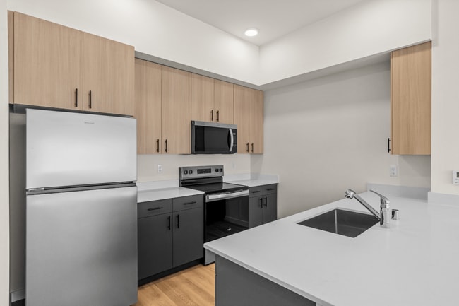 Cocina y recibe invitados con facilidad en una cocina moderna equipada con electrodomésticos de acero inoxidable, acabados elegantes y amplio espacio en la encimera. - 27 West Apartments