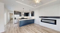 Located at 10 Candlelight Plz, this single-story home offers 4 bedrooms, 2 bathrooms, and a thoughtfully designed layout across one floor. The open-concept kitchen and living area serves as the heart of the home, showcasing dark shaker-style cabinetry, a bold navy kitchen island with a crisp white quartz countertop, stainless steel appliances, pendant lighting, and a wall-mounted fireplace with shiplap surround. Light wood-look flooring and a tray ceiling with a ceiling fan add visual depth and warmth to the shared living space. The four bedrooms are finished with plush carpet, crown molding, and windows that invite natural light. Each bedroom is served by dedicated closet space, with four closets total throughout the home. The two bathrooms are finished with light wood-look tile flooring and dark cabinetry. One bathroom features a tub-shower combo with black fixtures, while the other offers a standalone walk-in shower with a framed glass door. Both maintain a clean, modern aesthetic consistent with the rest of the home. A central hallway connects all rooms efficiently, making this home functional and cohesive in design.
