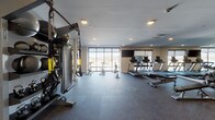 The fitness center at fifty58 is a thoughtfully designed, single-level workout facility that provides a comprehensive range of exercise options within a clean, contemporary environment. The space is laid out across two interconnected zones, allowing users to move seamlessly between cardio and strength training areas.

The cardio section is well-appointed with a row of treadmills, elliptical machines, stationary bikes, and a rowing machine, all positioned near large floor-to-ceiling windows that invite natural light and offer outdoor views. Wall-mounted flat-screen televisions are positioned throughout for added convenience during workouts.

The strength and functional training area features a multi-station cable machine, a TRX suspension system, a dumbbell rack with a full range of free weights, adjustable weight benches, medicine balls, and TRX-style resistance accessories. A water fountain is conveniently located within the space.

A dedicated open studio area provides ample room for stretching, yoga, or group exercise, enhanced by full wall mirrors that amplify the sense of space. The rubber-floored surfaces throughout provide durability and safety, while recessed lighting ensures consistent illumination across all zones. The overall ambiance is bright, functional, and well-maintained.