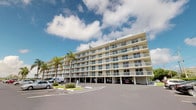 This property is situated within a well-established multi-storey coastal building, presenting a striking facade of clean, light-toned exteriors paired with a continuous run of private balconies across each level. The building's horizontal design and expansive glazing are characteristic of seaside architecture, allowing residents to take full advantage of the surrounding environment and open sky views. Mature palm trees frame the exterior, lending a relaxed, tropical character to the setting, while a generously proportioned on-site parking area provides convenient ground-level access. The covered ground floor supports the upper levels and offers sheltered parking beneath the building. Each balcony features glass or open balustrades, reinforcing the connection between interior living spaces and the outdoors. The overall presentation of the building suggests a well-maintained, resort-inspired environment suited to coastal living. The bright, airy exterior palette and the abundance of glazing throughout the facade point to interiors designed to maximize natural light and outdoor outlook. The surrounding landscaping and open skies complete the picture of a relaxed, sun-drenched coastal lifestyle.