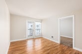 This single-floor residence offers a clean, functional layout with a neutral color palette and consistent finishes throughout. The open living area is highlighted by warm hardwood-style flooring that reflects natural light, and a set of glass French doors leads to a private balcony with views of the surrounding building exterior, bringing a sense of openness to the space.

The galley-style kitchen is efficiently designed with dark espresso cabinetry lining both sides, light quartz countertops, a subway tile backsplash, and a full suite of stainless steel appliances including a refrigerator, electric range, microwave, and dishwasher. Track lighting overhead ensures the space is well-lit throughout.

The bedrooms are carpeted for comfort and each features windows with blinds that allow for natural light and privacy. The rooms are generously proportioned and include baseboard heating. Neutral beige tones on the walls contribute to a calm and versatile ambiance.

The bathroom features large-format tile flooring in a rich brown tone, a standard tub-shower combination, and clean white fixtures. A hallway connects the rooms, providing a logical and accessible flow throughout the residence. Overall, the space presents a practical and move-in-ready environment with modern finishes.
