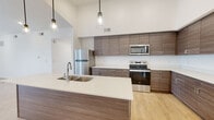 Located on Daro Drive in Herriman, Utah, this well-designed single-floor residence combines modern aesthetics with functional living spaces. The kitchen is a standout feature, showcasing dramatically high vaulted ceilings, rich wood-grain cabinetry extending floor to ceiling, crisp white quartz countertops, and a large center island with a double undermount sink. Stainless steel appliances, including a refrigerator, range, and microwave, complete the contemporary look, while pendant lighting adds warm ambiance. Light wood-tone flooring flows through the kitchen and into the spacious living area, which benefits from vaulted ceilings, recessed lighting, a ceiling fan, and sliding glass doors that open to an outdoor balcony. Bedrooms feature soft carpeting, generous closet space with double panel doors, and windows that frame open scenic views of the surrounding Utah landscape. Bathrooms are finished with wood-grain vanities, white quartz countertops, and light hardwood-style flooring. One bathroom includes a full tub-shower combination with classic subway tile surround, while another features stylish three-bulb vanity lighting. Throughout, the clean white walls and bright, neutral palette create a fresh, airy atmosphere that is both inviting and move-in ready.
