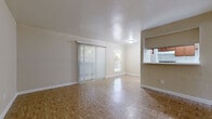 This single-story unit is defined by a consistent use of parquet flooring that extends through virtually every room, lending warmth and visual continuity across the entire layout. The living area is generously proportioned, with neutral beige walls and a sliding glass door dressed in vertical blinds that allows natural light to filter in while providing access to the outdoors. A pass-through opening connects the living space directly to the kitchen, enhancing the sense of openness between the two areas.

The galley-style kitchen is efficiently arranged, featuring dark wood cabinetry on both sides, a coil-burner range, a full-size refrigerator, and a sink with counter space on the opposite wall. Light-toned parquet tile lines the kitchen floor, complementing the cabinetry tones.

The bedrooms are well-sized and bright, each finished with the same parquet flooring and neutral walls. One bedroom benefits from a window with outdoor views, while another includes wall-mounted climate control. A spacious walk-in closet with built-in shelving provides ample storage.

The bathroom is clean and straightforward, featuring a tiled tub-shower combination, a wood-toned vanity, and parquet flooring, maintaining a cohesive aesthetic throughout the unit.