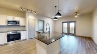 Located in Grapevine, TX, this thoughtfully designed 2-bedroom, 2-bathroom residence offers a comfortable and modern single-floor layout. The open-concept kitchen and living area serves as the heart of the home, anchored by a granite-topped island with an integrated sink and stylish pendant lighting overhead. The kitchen is outfitted with crisp white shaker cabinets, a herringbone tile backsplash, stainless steel appliances, and track lighting, creating a clean and functional workspace. Wood-look flooring flows throughout the main living areas, complementing the bright, neutral palette. French doors in the living room invite natural light and provide access to a private outdoor balcony with neighborhood views. The spacious primary bedroom features wood-look flooring, a ceiling fan, and connects to an en-suite bathroom with a glass-enclosed shower and a walk-in closet with wire shelving. The second bedroom is carpeted for comfort, equipped with a ceiling fan, and receives natural light through a window with views of the surroundings. The second bathroom includes a soaking tub with a tiled surround. A hallway with frosted glass accents and two closets rounds out this well-organized and inviting residence.