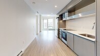 Located at 333 E 11th Ave in Vancouver's Mount Pleasant neighbourhood, this well-appointed two-bedroom, two-bathroom unit offers a thoughtfully designed single-level layout. The open-concept kitchen and living area anchors the space, featuring light wood-look flooring, recessed lighting, and a sleek modern kitchen outfitted with stainless steel appliances, a smooth cooktop, integrated cabinetry in a cool grey tone, and a clean white countertop. The layout flows efficiently from the entry toward a bright living area with a large window framing views of the surrounding cityscape. Both bedrooms are finished with the same light hardwood-style flooring and neutral walls, with one bedroom showcasing a floor-to-ceiling window offering elevated views of Vancouver, while the other features practical sliding panel closet doors that maximize space. The two bathrooms maintain a clean, contemporary aesthetic — one includes a soaker tub with an overhead shower and white tile surround, while the other offers a floating vanity with a bright mirror and natural light from a window. An in-unit laundry area adds everyday convenience. Throughout, the unit presents a cohesive, minimalist palette of whites and warm neutrals, creating a bright and functional urban living space.