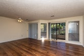 This single-floor residence in Columbus, Georgia offers a practical and well-organized layout across several distinct living areas. The open living and dining area is one of the home's most notable spaces, featuring dark wood-look flooring that extends throughout the main living zones. A sliding glass door floods the living room with natural light and provides access to an outdoor area, while a second set of sliding doors leads to the dining room, which is distinguished by an elegant chandelier that adds a refined touch to the space.

The kitchen is designed with functionality in mind, featuring a pass-through counter with a granite-style surface that connects it to the adjacent living area. Warm wood cabinetry lines the walls, and black appliances including a range, microwave, and refrigerator are included. A dedicated laundry nook with hookups is also conveniently located within the unit.

The bedrooms are carpeted for comfort and receive natural light through blinded windows, with ceiling light fixtures providing additional illumination. The bathroom includes a granite-topped vanity with wood cabinetry, a mirror, and a full tub-shower combination with a grab bar, all finished with wood-look flooring for a cohesive aesthetic throughout the home.
