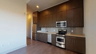 Located at 3410 Alexander Rd in Atlanta, GA 30326, this modern single-floor residence showcases a clean, contemporary design with consistent finishes throughout. The open-concept kitchen is a standout feature, equipped with rich dark-wood cabinetry extending floor to ceiling, light stone countertops, a subway tile backsplash, and a full suite of stainless steel appliances including a gas range, built-in microwave, dishwasher, and refrigerator. Durable wood-tone flooring runs throughout the main living areas, lending warmth and cohesion to the space. Large windows in the living area and bedroom flood the interior with natural light and offer open views of the surrounding Atlanta landscape, creating a bright and airy ambiance. The bedroom benefits from corner window placement, maximizing both light and views. The bathroom is finished with a dark wood vanity, white quartz countertop, a large mirror with overhead lighting, tile flooring, and a walk-in shower. A hallway connects the rooms and includes louvered closet doors and built-in open shelving, providing practical storage solutions. A sliding glass door leads to a private balcony, extending the living space outdoors. The overall design emphasizes clean lines, neutral tones, and functional modern living.