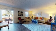 This well-appointed single-floor residence offers a thoughtfully laid-out interior with a warm, coastal-inspired aesthetic. The living room serves as a welcoming centerpiece, featuring wood-look flooring, wainscoting, multiple windows that invite natural light, and comfortable seating arranged around a distinctive trunk-style coffee table. Tropical artwork and colorful accent pillows lend the space a relaxed, inviting character.

The dining area flows naturally from the living space and is highlighted by sliding glass doors that open to an outdoor patio, offering pleasant views and easy indoor-outdoor access. Adjacent to the dining area, the kitchen is efficiently organized with ample white cabinetry, full appliances including a refrigerator, range, microwave, and dishwasher, along with a pass-through window and wood-look flooring.

The primary bedroom is generously sized with plush carpeting, a bold red dresser, and direct access to an en-suite bathroom and a walk-in closet. A second bedroom accommodates twin beds and features built-in closet storage, making it ideal for guests. Two full bathrooms, each with a tub-shower combination, serve the home. The overall ambiance is bright, cohesive, and comfortably furnished throughout.