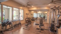 Located at 1001 Bolling Ave in Norfolk, Virginia, this single-level fitness center is thoughtfully designed to support a full range of workout routines. The space is bathed in natural light, courtesy of large windows that line multiple walls, offering views of the surrounding greenery and creating a bright, energizing atmosphere throughout.

The facility is organized into distinct functional zones. A dedicated cardio area houses a row of SportsArt elliptical trainers and multiple treadmills, all positioned to face the windows and take advantage of the outdoor views. Adjacent to this is a strength training section equipped with a multi-station cable machine, adjustable benches, and a comprehensive free weight area featuring a full rack of dumbbells. Floor-to-ceiling mirrors along the walls enhance the sense of space and allow for proper form monitoring.

An open-concept exercise studio provides ample room for stretching, functional fitness, and group workouts. This area includes a wall-mounted flat-screen TV, exercise balls, a mounted mat board, and a ceiling fan — lending both functionality and comfort. Durable, easy-to-clean speckled flooring runs throughout the entire facility, ensuring safety and resilience under heavy use.

Ceiling fans are distributed across the space to maintain airflow, and recessed lighting supplements the generous natural light. Motivational wall decals reinforce the health and wellness theme, making this fitness center an inviting and practical environment for all levels of exercise.